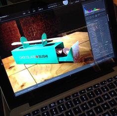 an open laptop computer sitting on top of a wooden table next to a cupcake box