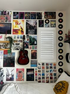 a bedroom wall covered in various records and vinyls, with a guitar on the bed