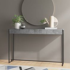 a modern console table with a round mirror on the wall above it and potted plants next to it