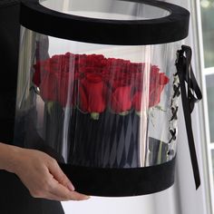 a woman is holding a clear box with red roses in it and black ribbon around the bottom