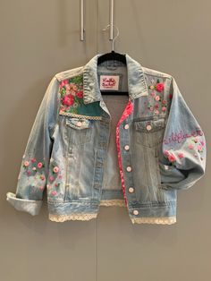 a denim jacket with flowers on it hanging from a hanger in front of a wall