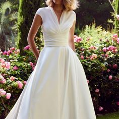 a woman wearing a white dress standing in front of flowers