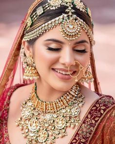 a woman in a red and gold bridal outfit with jewelry on her head, smiling