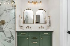 a bathroom with marble counter tops and green cabinetry, along with two mirrors on the wall