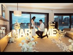 a man kneeling down next to a woman in front of a room filled with flowers