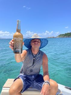 a man wearing a blue hat and holding up a bottle of beer on a boat