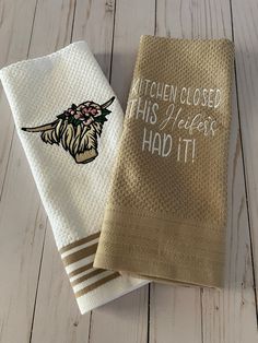 two kitchen towels with embroidered words on them sitting on a white wooden floor next to each other