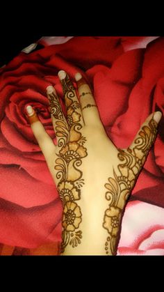 a woman's hand with henna on top of red fabric next to a rose