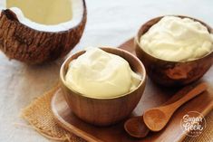 two coconuts with cream in them on a wooden tray