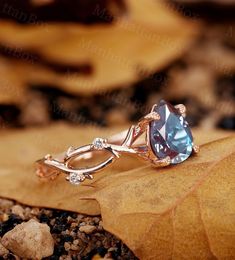 an engagement ring with a blue topazte surrounded by leaves and rocks on the ground