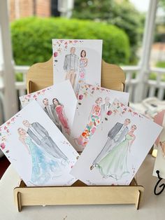 some cards are sitting on a table with flowers and pictures in the middle one has a bride's dress