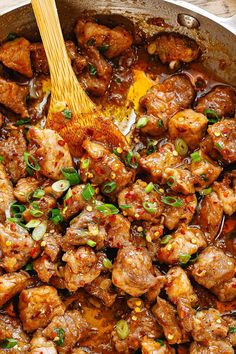 a pan filled with meat and vegetables on top of a wooden table next to a spoon