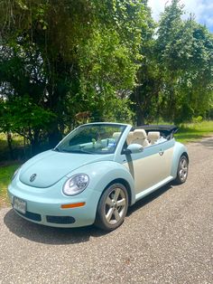 a blue convertible car is parked on the side of the road in front of some trees