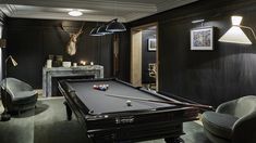 a pool table in the middle of a living room with chairs and lamps on either side