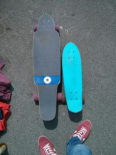 two skateboarders standing next to each other on the ground with their feet propped up