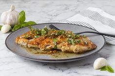 a plate with some chicken on it next to garlic and green leaves in the background