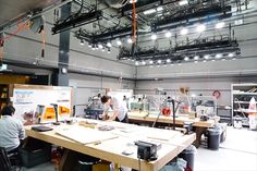 two people working in an industrial building with lots of lights and equipment on the ceiling