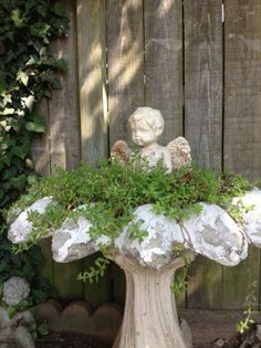 a statue sitting on top of a white planter filled with green plants next to a wooden fence