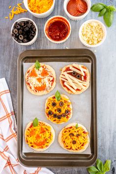 four mini pizzas on a baking sheet with toppings and sauces around them