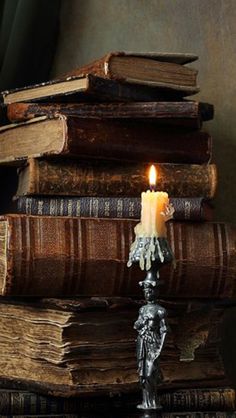 a stack of books sitting on top of a table next to a candle