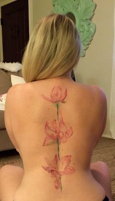 a woman sitting on the floor with her back turned to the camera and showing off her pink flower tattoo