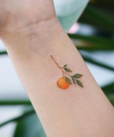 an orange tattoo on the wrist of a woman's arm, with leaves around it