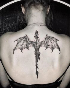 the back of a woman's shoulder with a dragon tattoo on it and wings