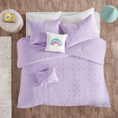 a bed with purple sheets and pillows on top of it next to a white rug