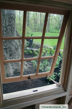 an open window in the corner of a room with a view of trees and grass