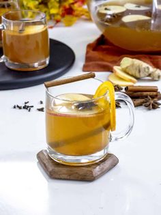 two mugs filled with tea and cinnamon on top of a white table next to other items