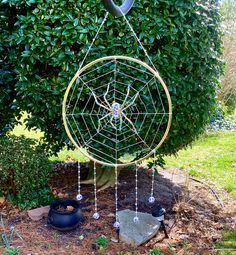 a metal circular object with beads hanging from it's sides in front of a tree