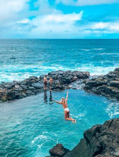 two people standing in the water near rocks and an open area with blue water on both sides