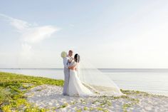 a bride and groom standing on the beach with their arms around each other as they kiss