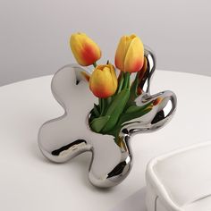 some yellow tulips are in a silver vase on a white table with a bowl