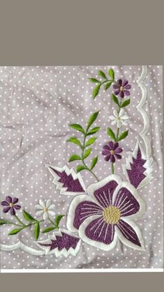 a purple and white flower with green leaves on a polka doted fabric background that looks like it has been embroidered onto