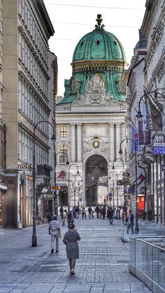 people are walking down the street in front of some buildings and an ornate building with a green dome on top