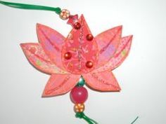 an ornament made out of paper and beads on a green string with a red flower