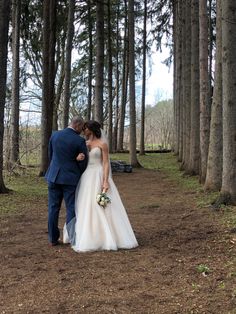 a bride and groom walking through the woods