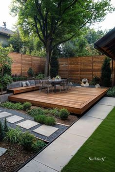 a wooden deck in the middle of a yard with grass and plants around it, surrounded by trees