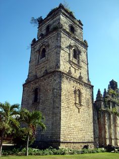 an old stone tower stands in the middle of a grassy area next to palm trees