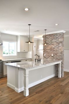 a large kitchen with an island in the middle and brick on the wall behind it