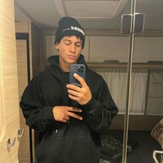 a young man taking a selfie in the bathroom with his cell phone while wearing a hat