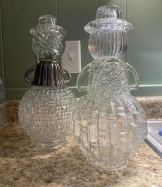 two clear glass vases sitting on top of a counter next to a light switch