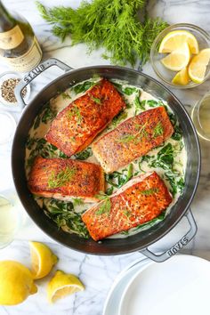 three salmon fillets in a pan with spinach and lemons on the side