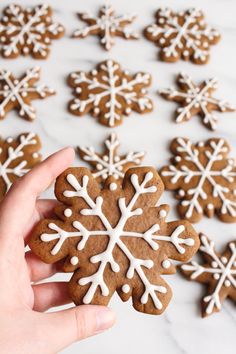 a hand holding a gingerbread snowflake cookie in front of several other cookies