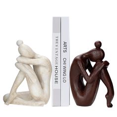 two figurines sitting next to each other in front of a white box and book