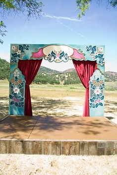 an outdoor stage set up with red curtains and pink drapes on the sides, in front of a field