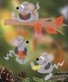 three koalas hanging from a tree branch with leaves and acorns in the background