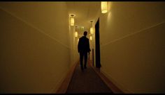 a person walking down a long hallway with lights on either side of the door and in between them