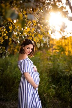 a pregnant woman standing under a tree with the sun shining through her hair and wearing a striped dress